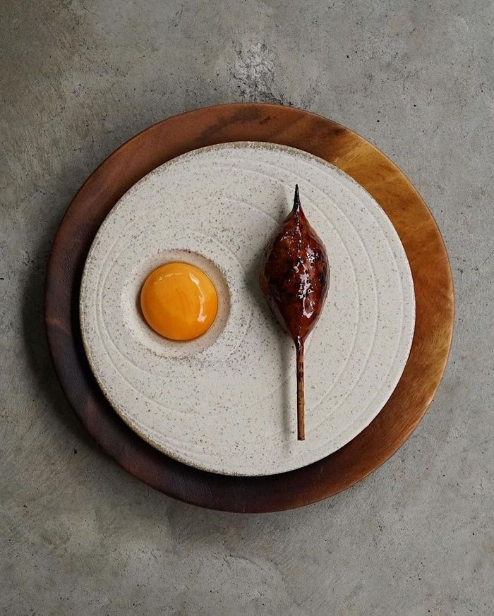 An egg yolk and a glazed skewer on a stoneware plate