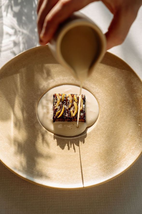 Sauce being poured over a dish on a stoneware plate
