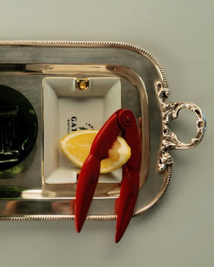 A silver serving tray with a lemon wedge and a red lobster cracker